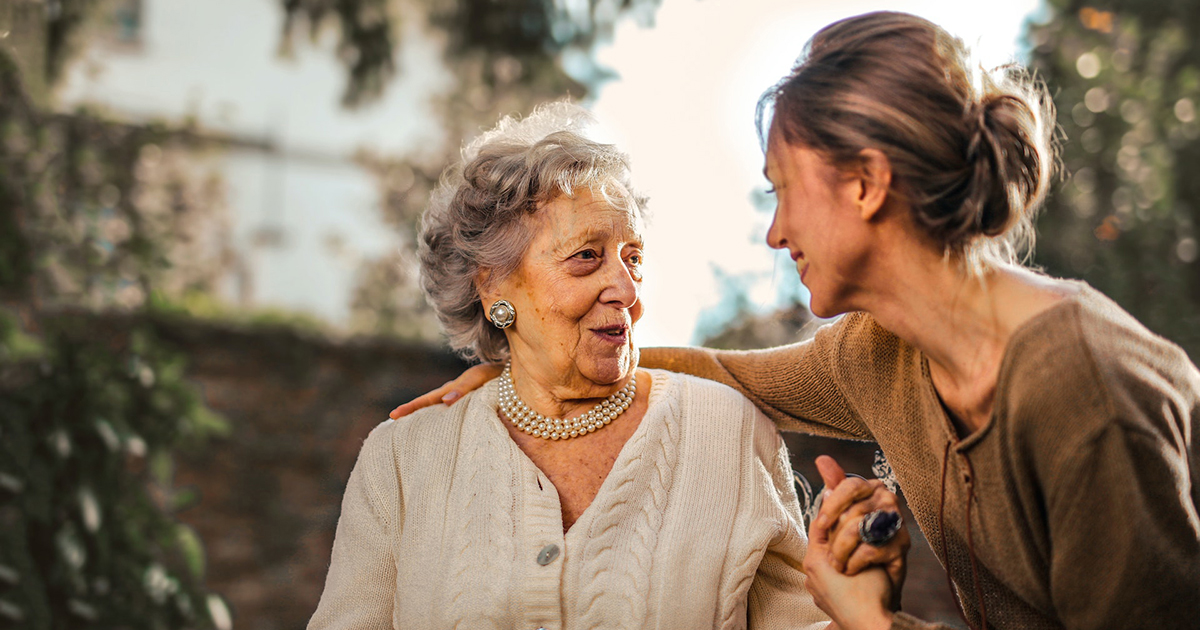 Photo of an older woman smiling at a younger woman who has her hand on the older woman's shoulder.