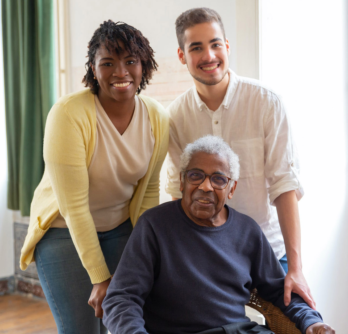 Photo of an older man sitting in a wheelchair flanked by a younger man and woman. All are smiling and happy.