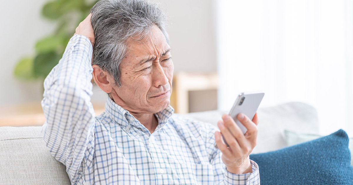 Photo of an older man squinting in confusion at his smartphone.