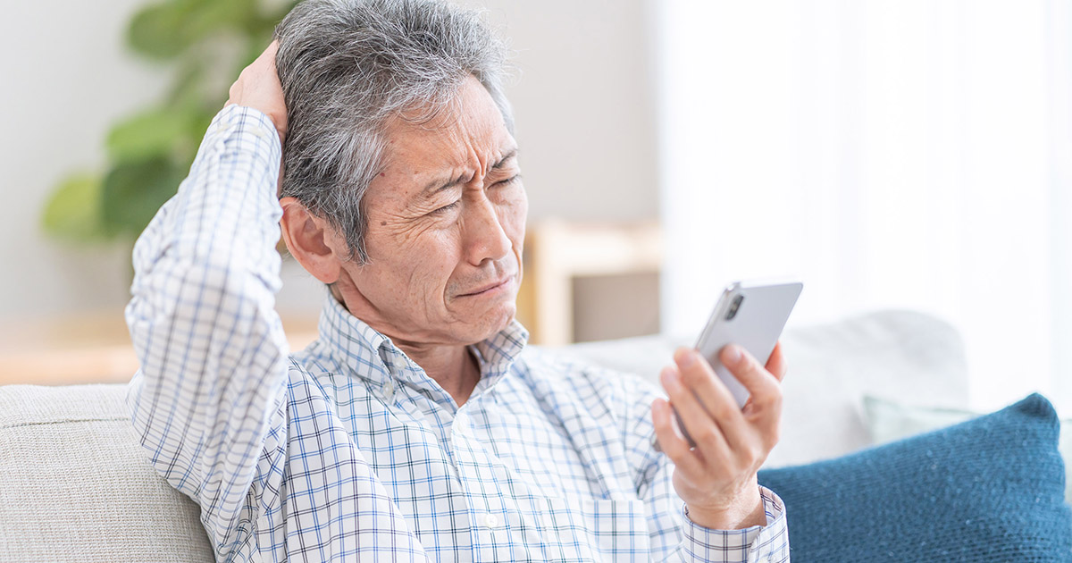 Photo of older man sqinting at his smart phone in confusion.