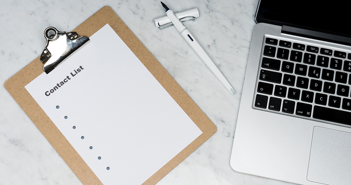 Photo of a clipboard with a contact list on it, a pen, and a laptop.