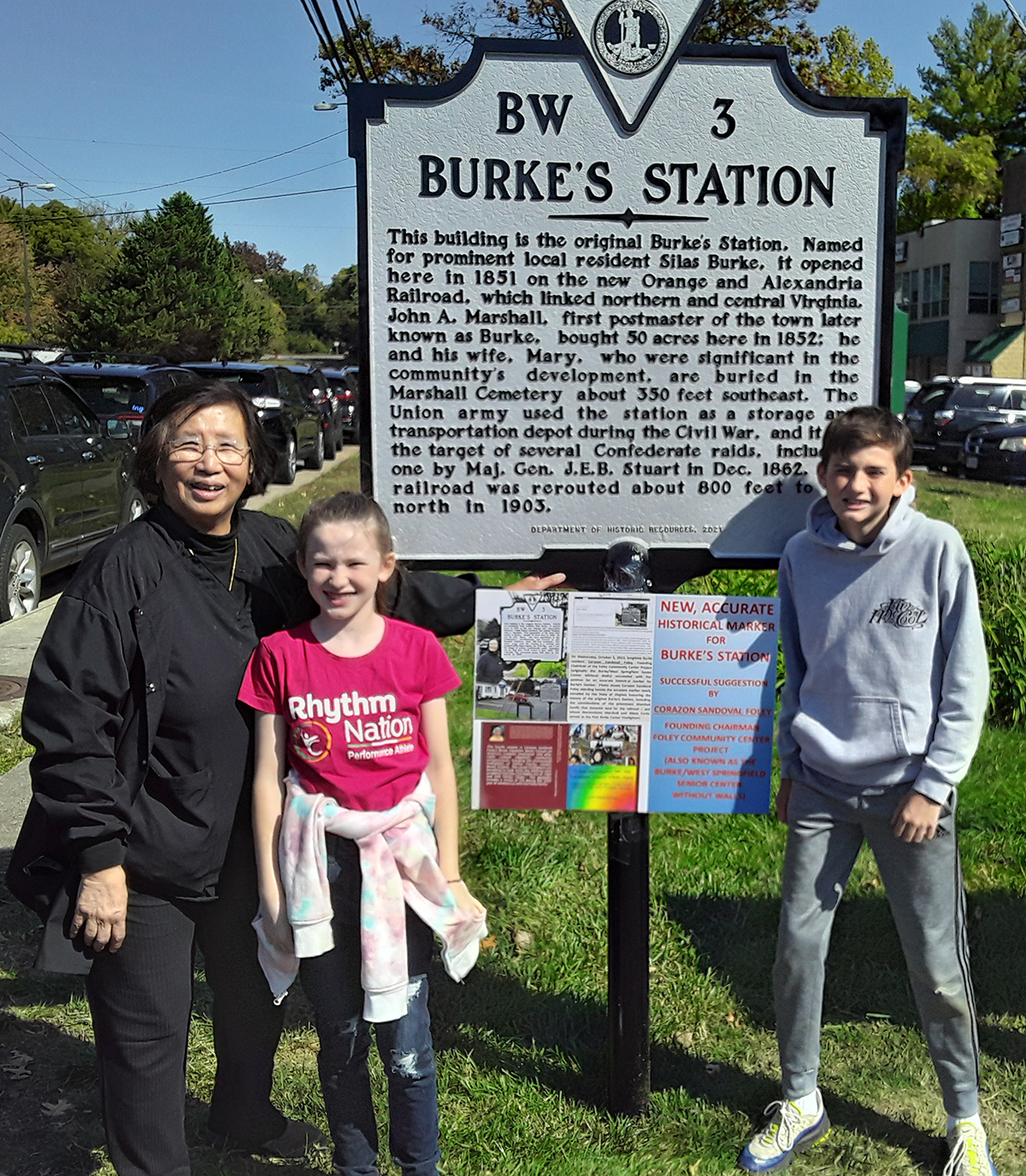 Corazon Sandoval Foley with grandchildren Ciara and Daniel in front of the Burke's Station historical marker.