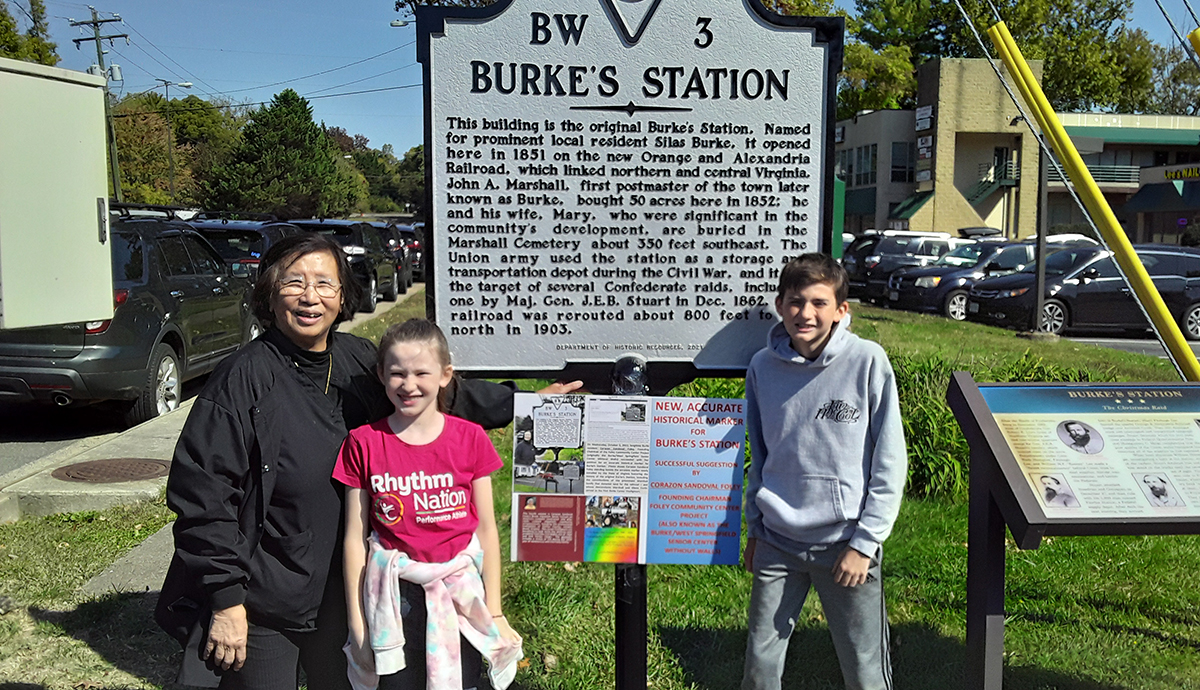 Photo of Corazon Sandoval Foley standing in front of the Burke's Station historical marker with grandchildren Ciara and Daniel.