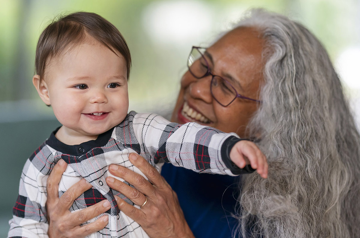 Photo of an older woman smiling and holding a smiling toddler.