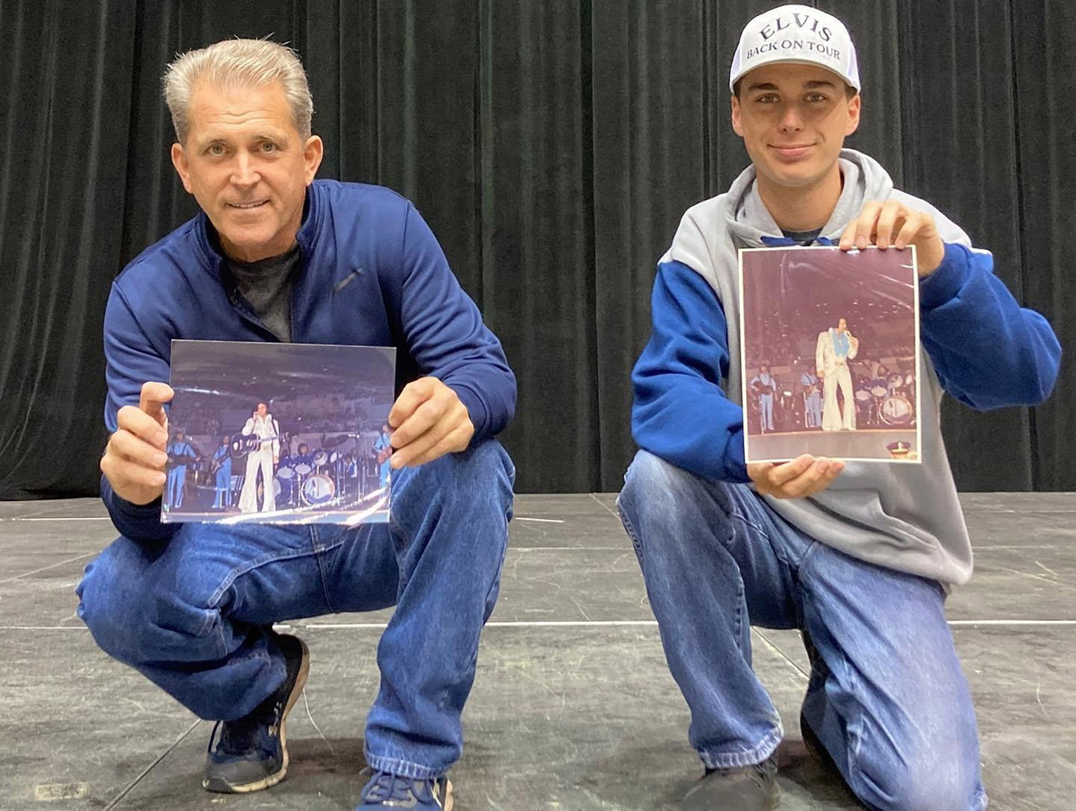 Jay and Michael Corwin posing on a stage holding photos of Elvis Presley performing. 