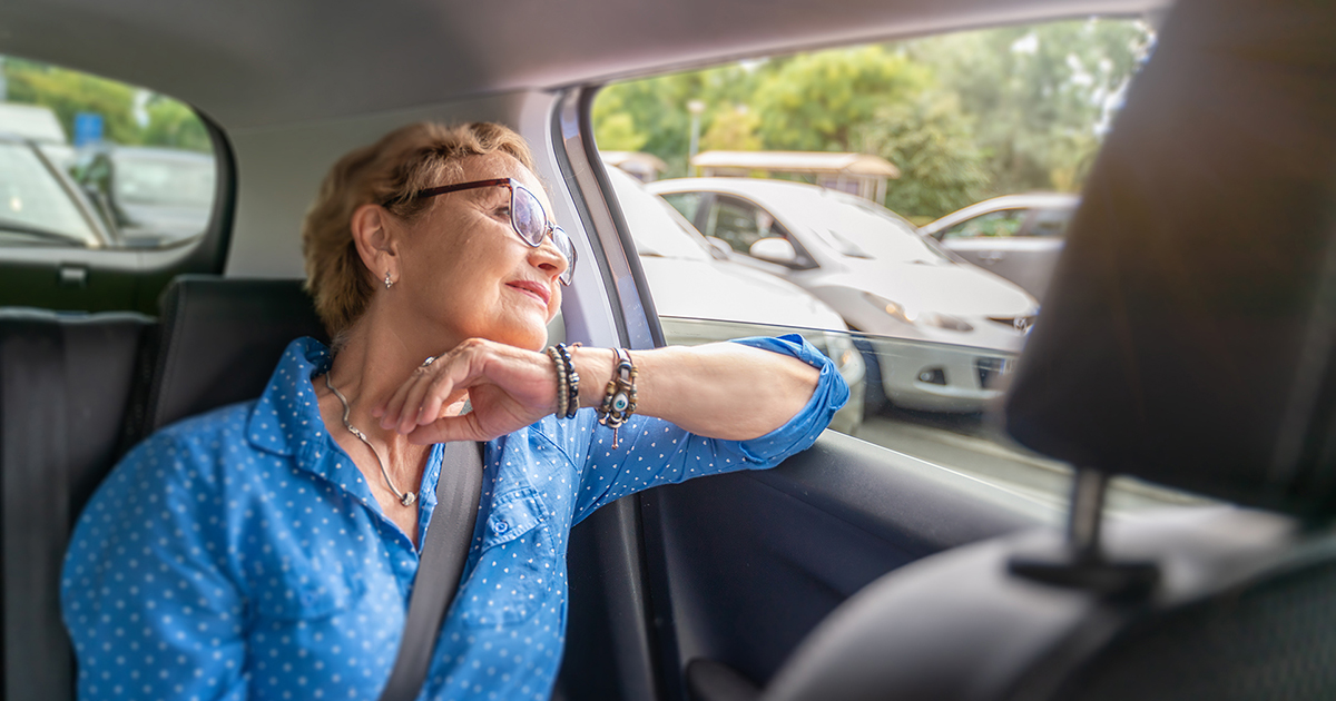 Photo of an older woman riding in the backseat of a car gazing out the window.