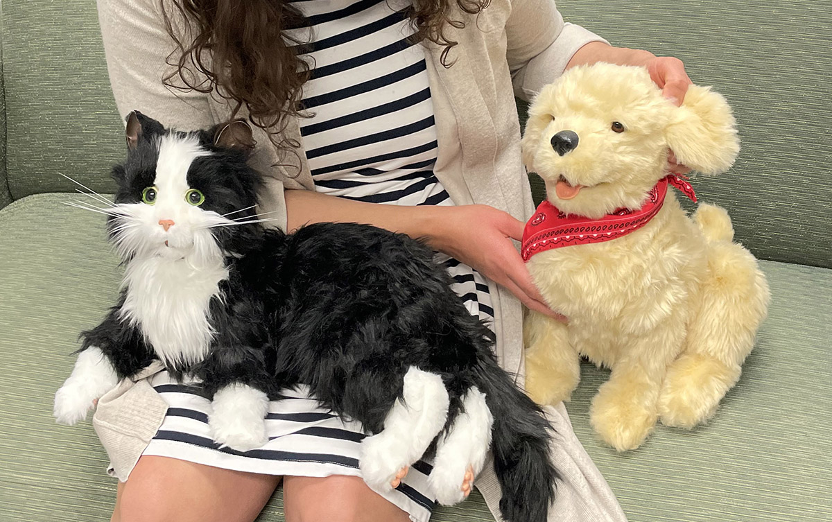A Volunteer Solutions employee holding a robotic cat and robotic dog in her lap.