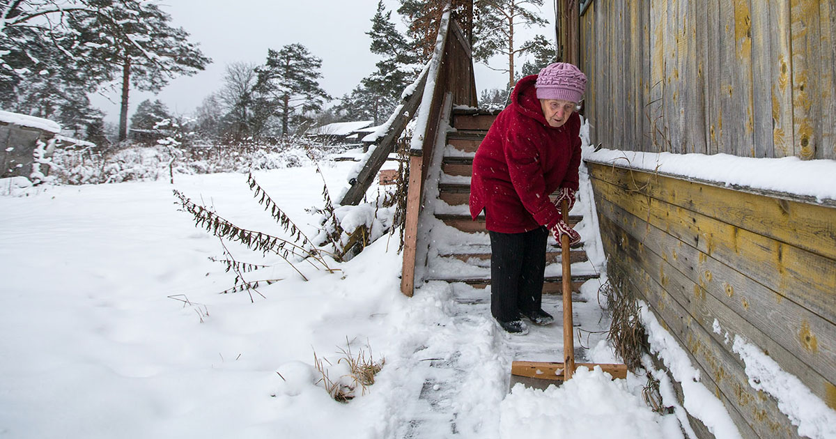 Photo of an older woman shoveling snow-covered steps.