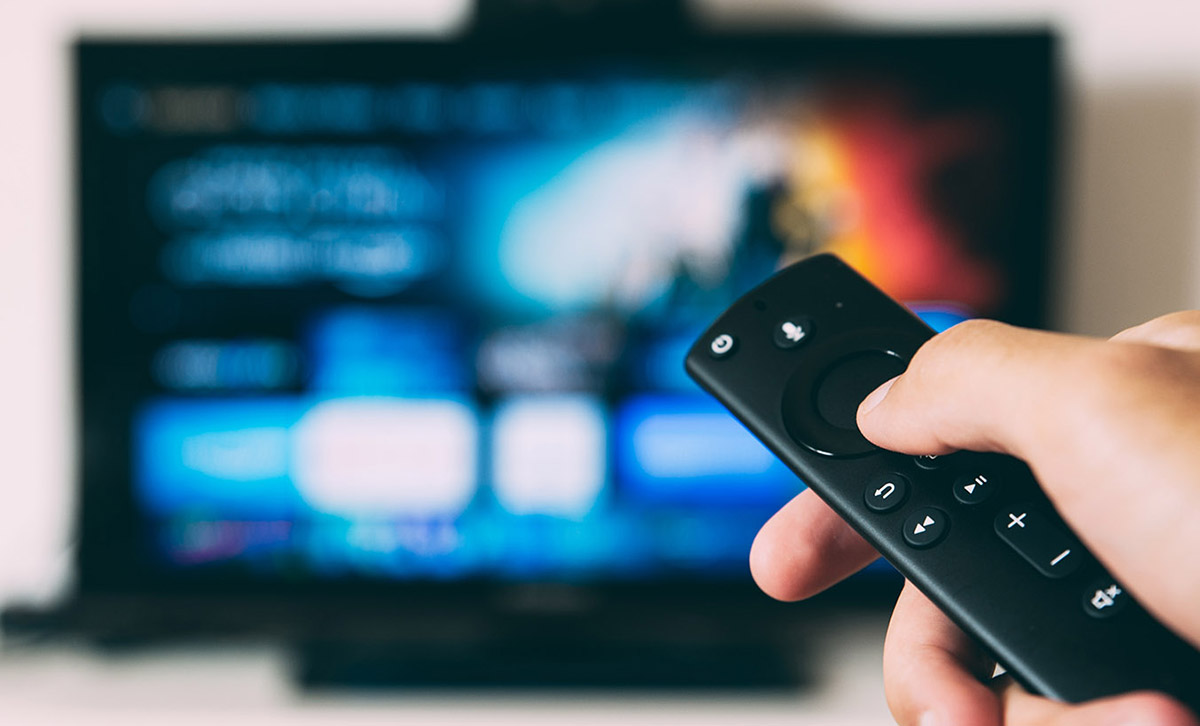 Photo of a hand holding a remote control pointing at a smart TV.