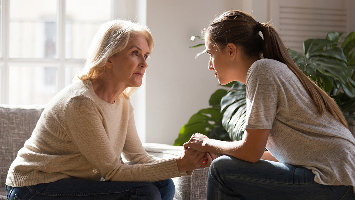 Photo of an older woman holding hands with a teen girl while they talk