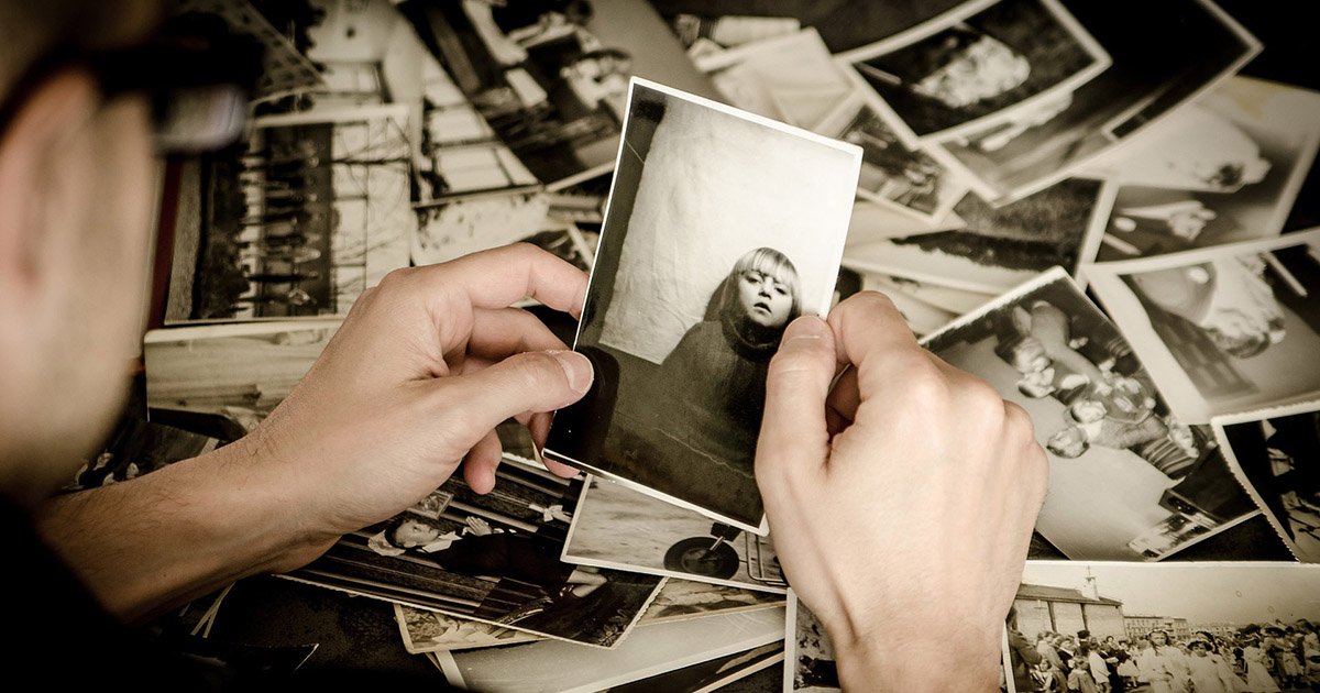 A man holding a photo of a young girl, selected from a tabletop covered in old family photos.
