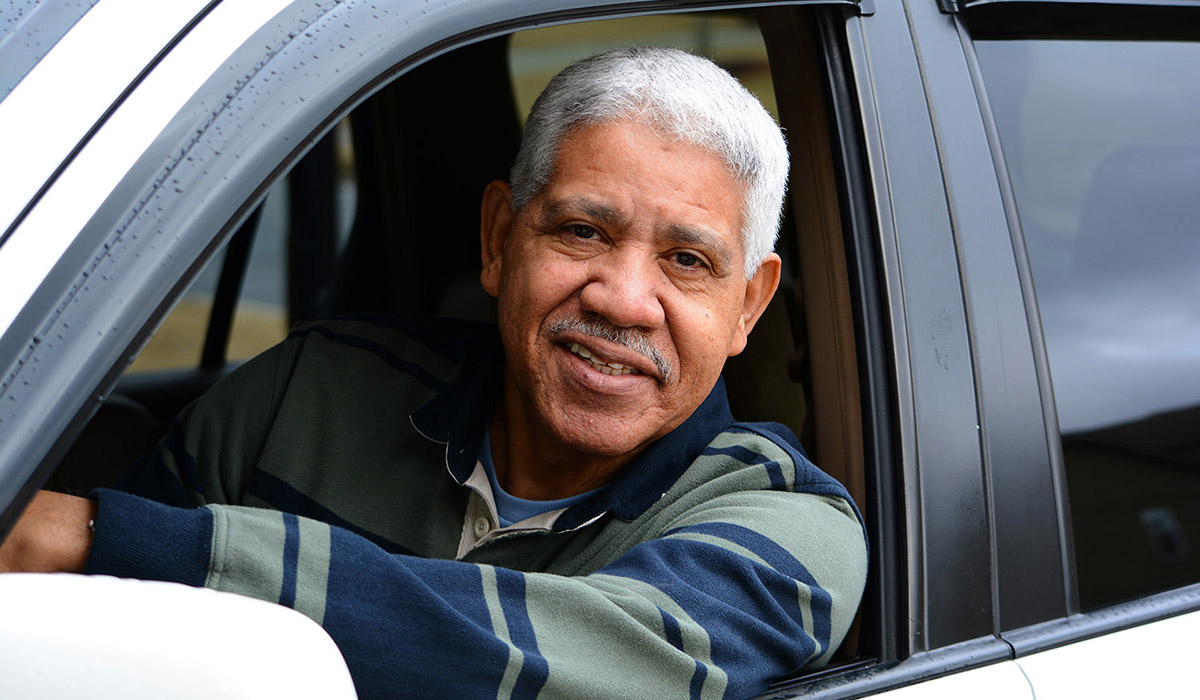 Photo of a man sitting in the driver's seat of a car, smiling and looking out the window.