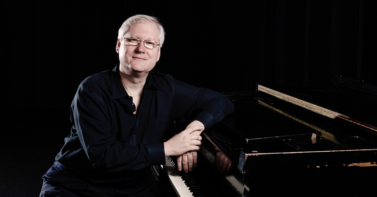 Photo of Christopher Johnston seated at a piano dressed in black. 