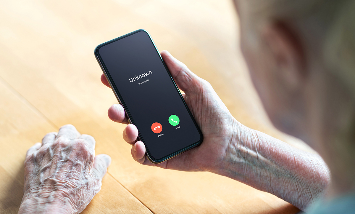 Photo of an older woman holding a smartphone with the screen displaying an incoming call from an unknown caller.