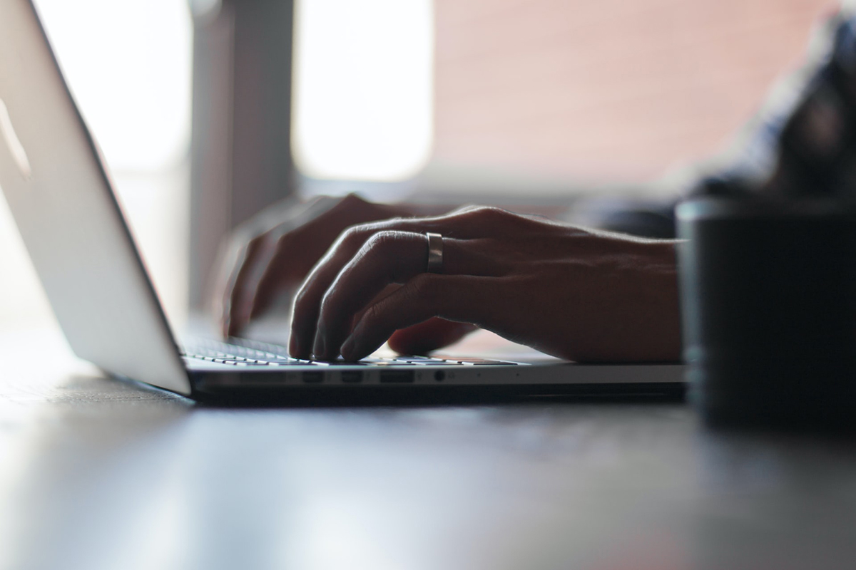 Photo of a pair of hands typing on an open laptop.