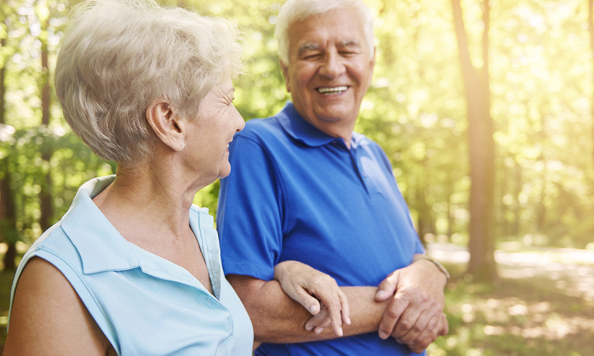Photo of an older couple smiling while walking outdoors together.