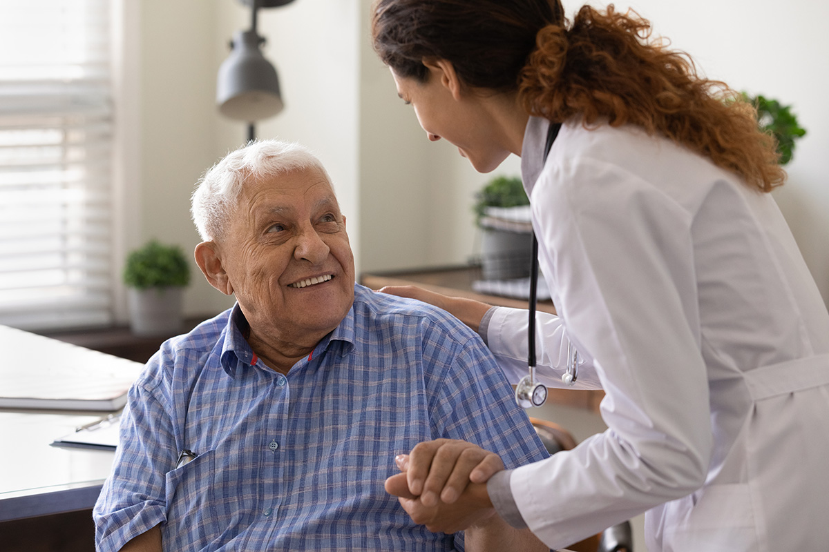 Photo of an older man holding hands and smiling at a woman dressed in a lab coat.