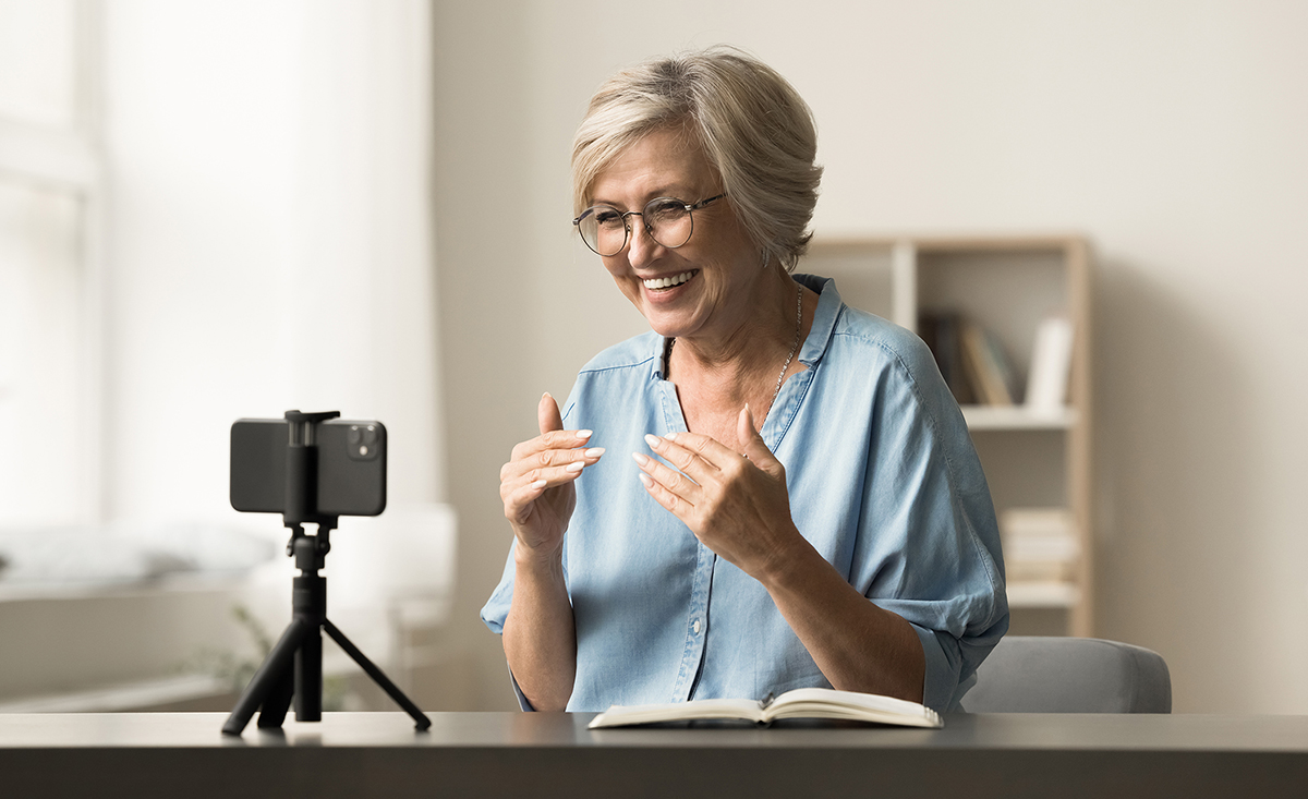 Photo of an older woman facing the camera with a support group gathered in the background.