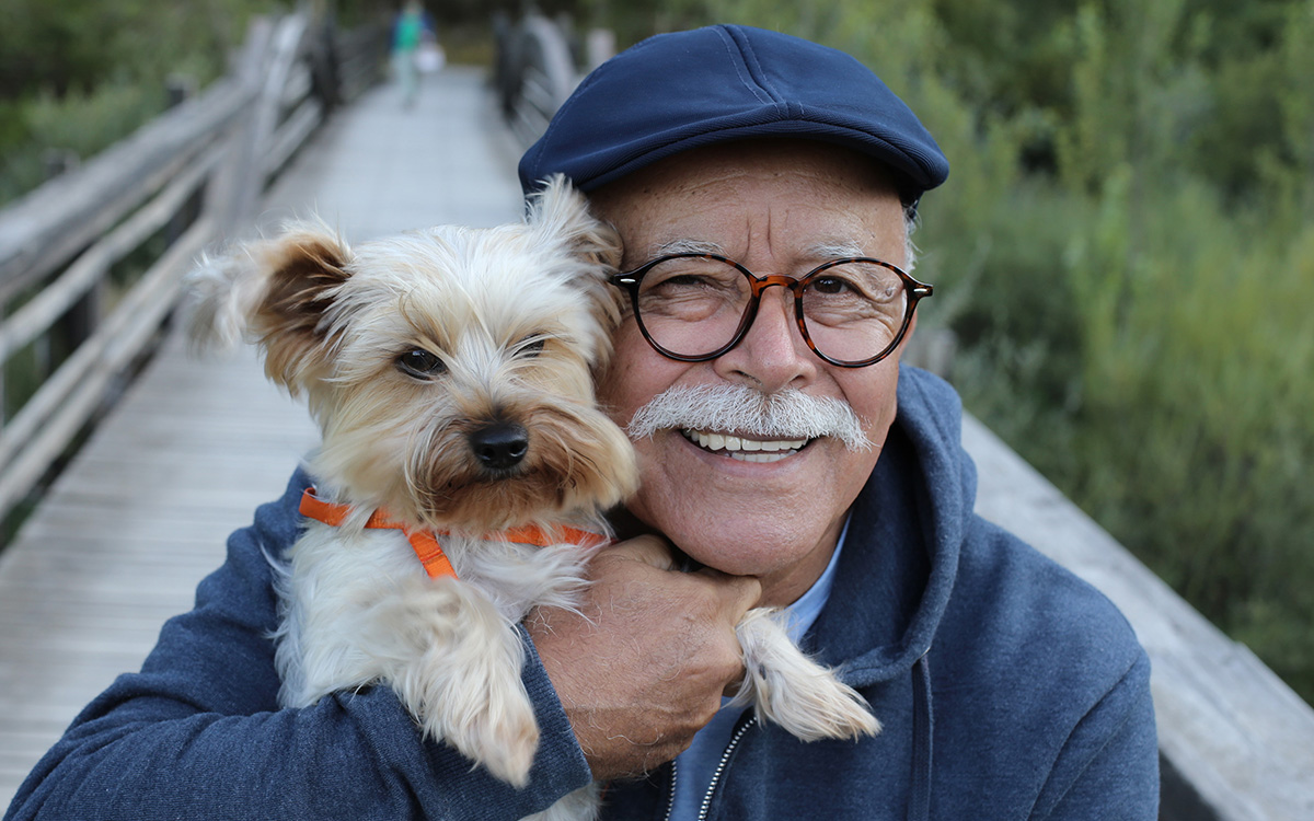 Photo of an older man holding his dog and smiling while on a walk outdoors.