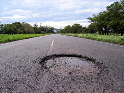 Photo of a road with a big pothole.