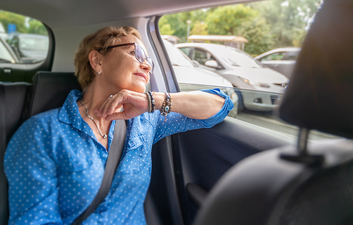 Photo of an older woman seated in the backseat of a car looking out the window. 