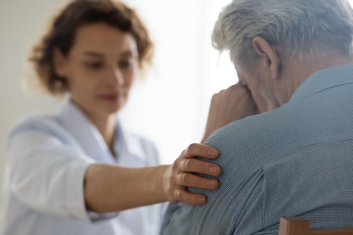 Photo of a woman attempting to comfort a weeping older man by gently resting her hand on his arm.