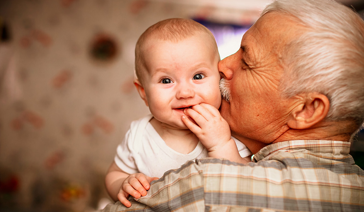 A smiling baby is held in the arms of an older man.