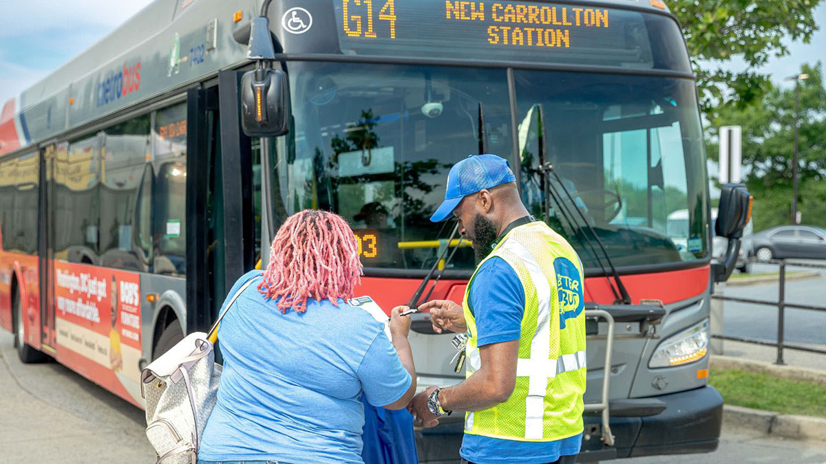A WMATA employee helps a customer as they stand next to a metro bus.