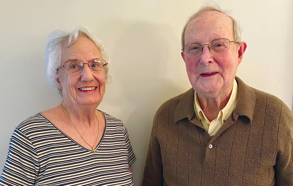 Photo of Gladys and Cap Oliver standing in front of a blank wall in their home and smiling.