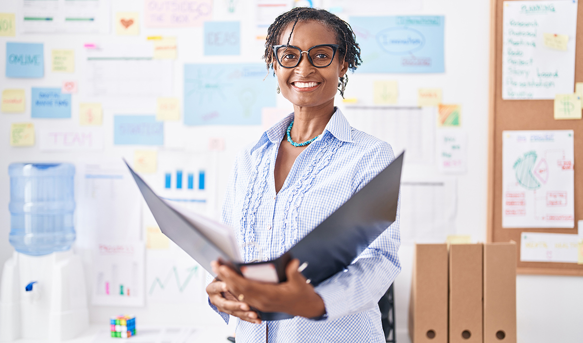 Smiling African American woman stands in a room holding an open binder.