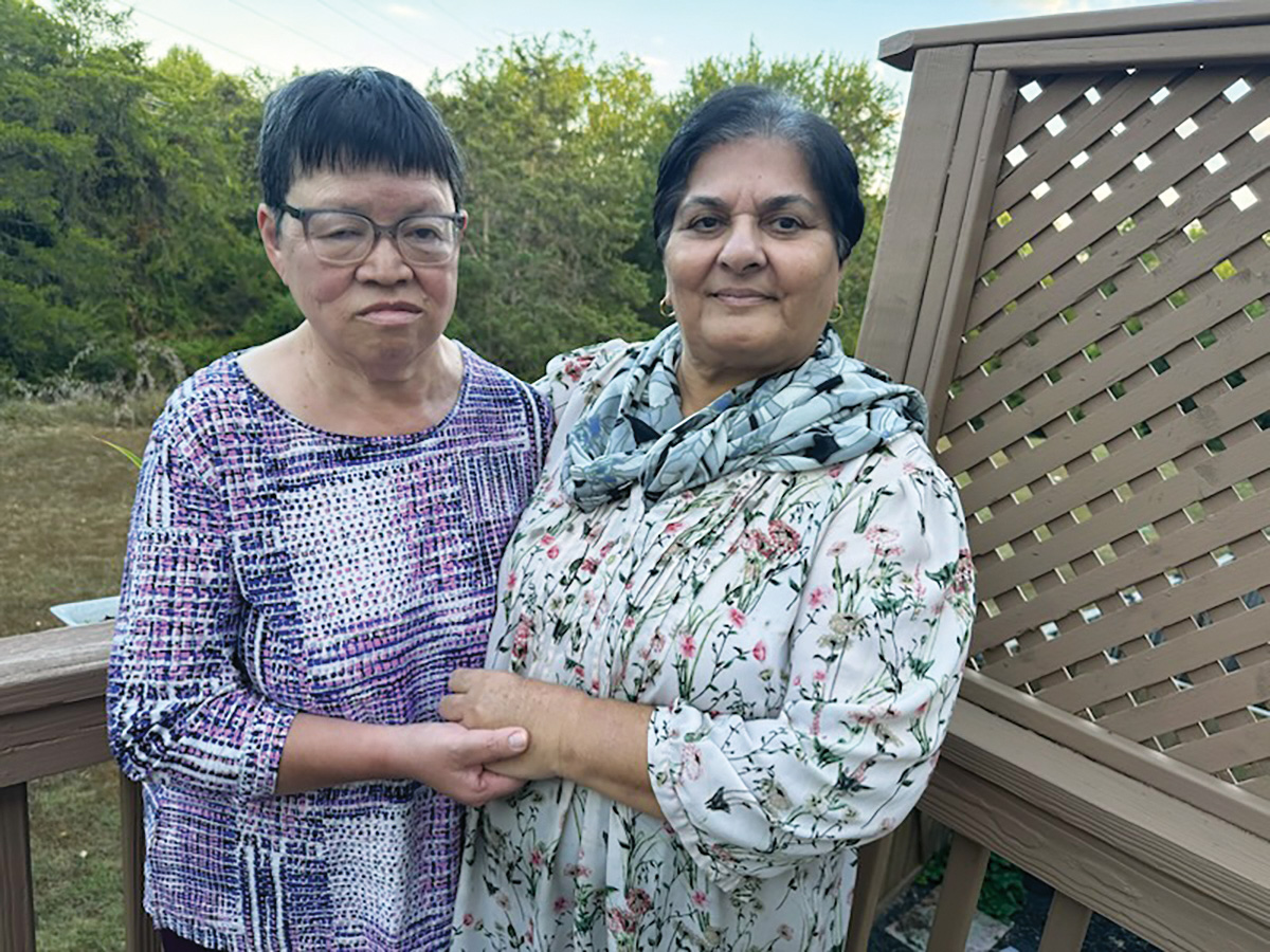 Catherine and Rubina stand outdoors on a deck holding hands.