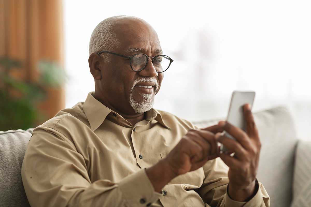 An older man smiles while looking at the screen of his phone.