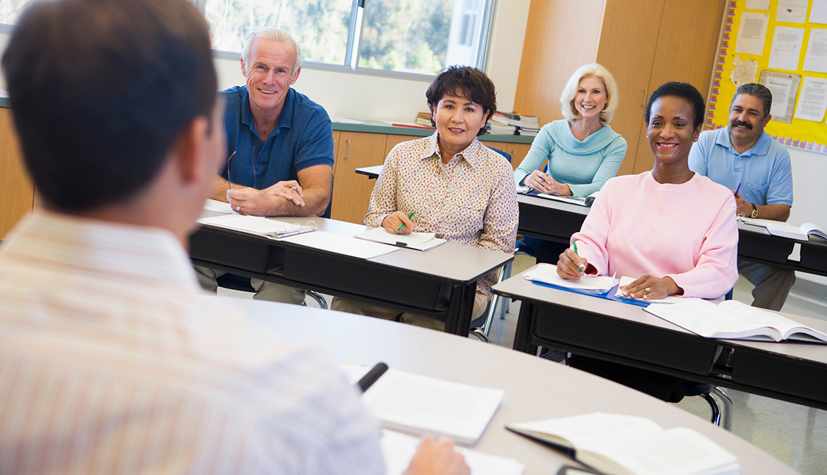 A teacher faces a classroom of older adults seated at tables. 