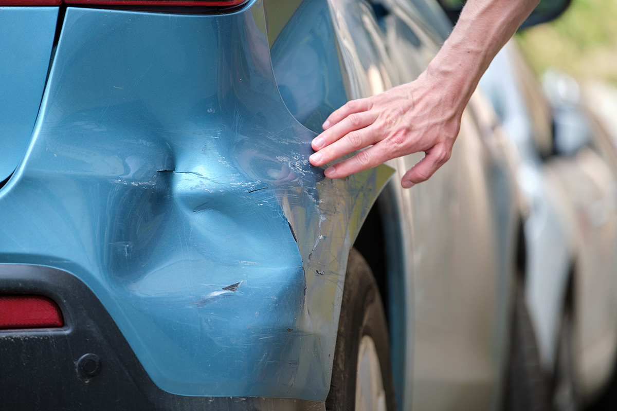 Someone running their hand over the dented and scratched back panel of a blue car.