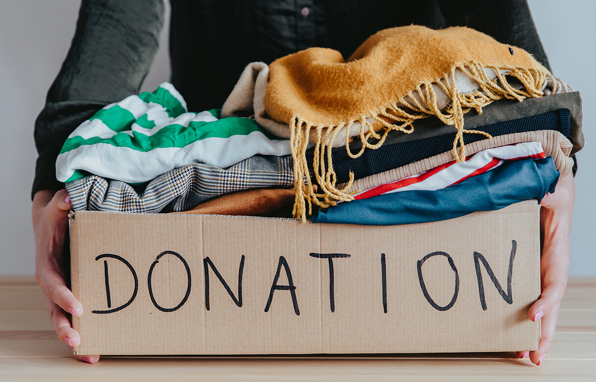 Photo of a person holding a box of folded clothing. The boxed is labeled with the word "donation."