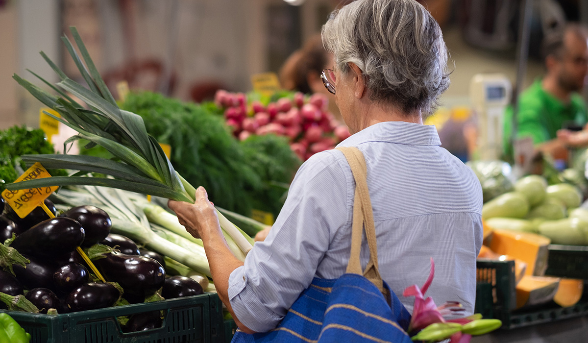 An older woman shops for vegetables at a farmers market stand.