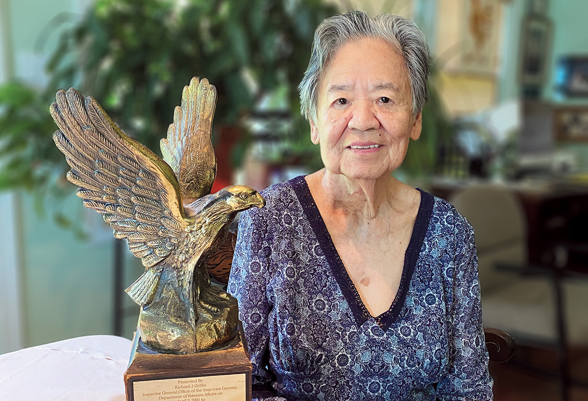 Fidelita Levy seated in her home. Displayed on the table next to her is her Golden Eagle Award.