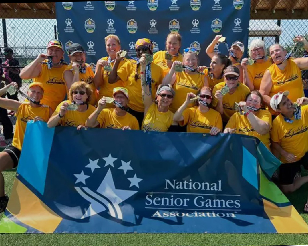 Members of the Golden Girls softball team pose for a photo while holding up their medals and smiling. 