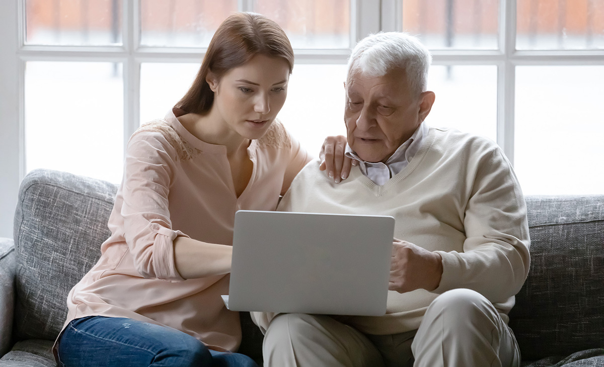 A young woman and older man sit on a sofa looking at a laptop.