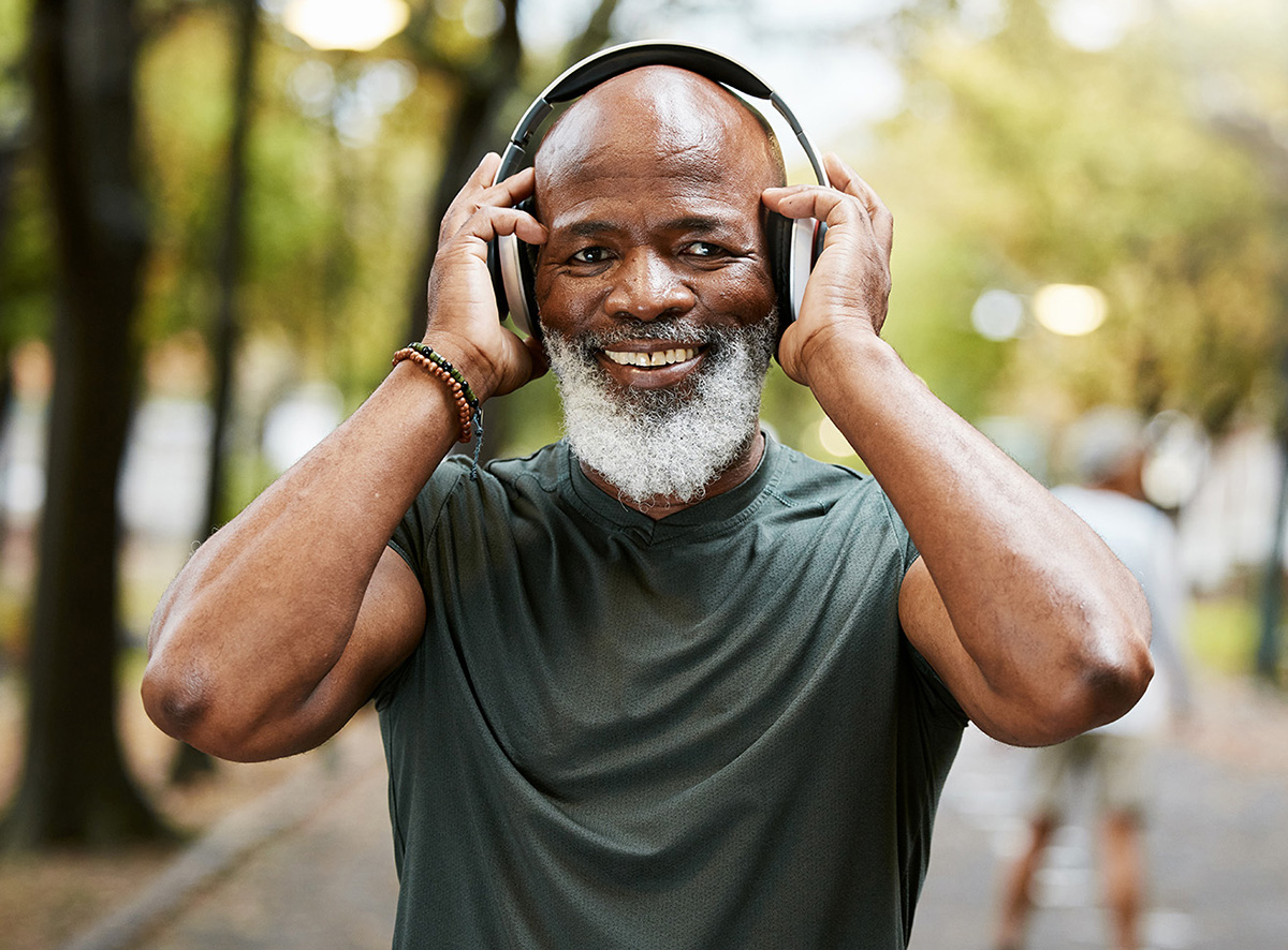 A smiling older African American man adjusts his headphones while walking outdoors.