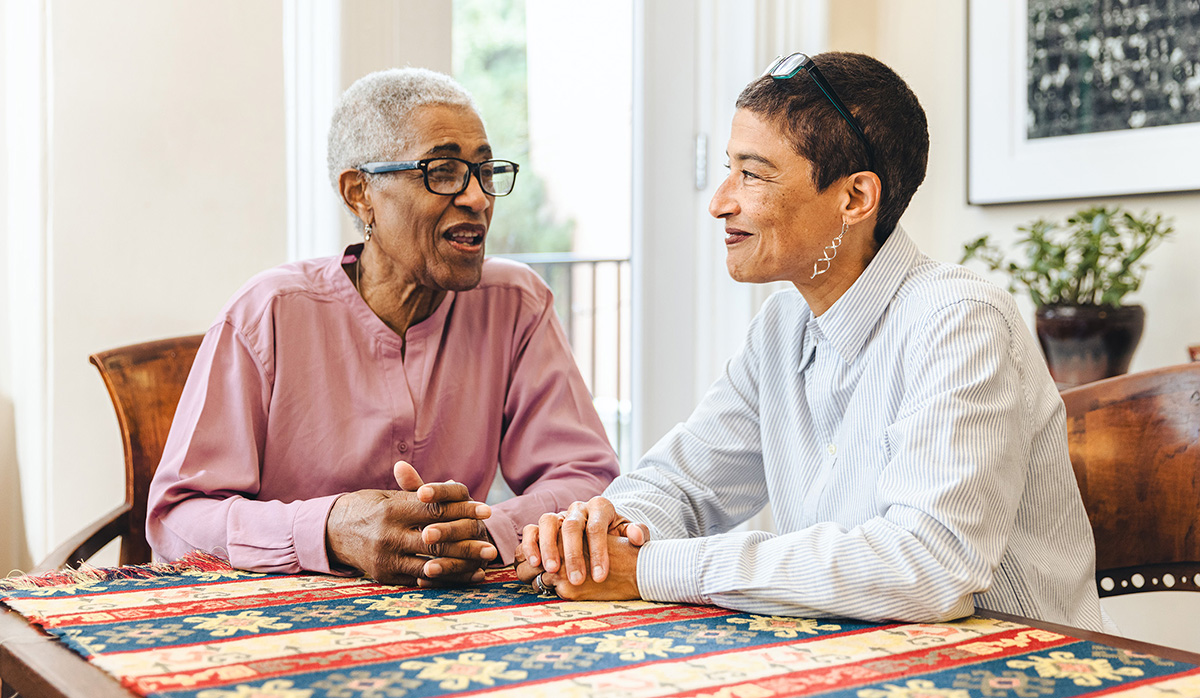 An older African American mother and her daughter sit at a table talking.