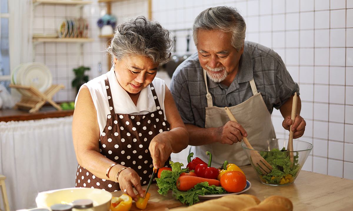 An older Asian couple prepares a salad together in their kitchen. 