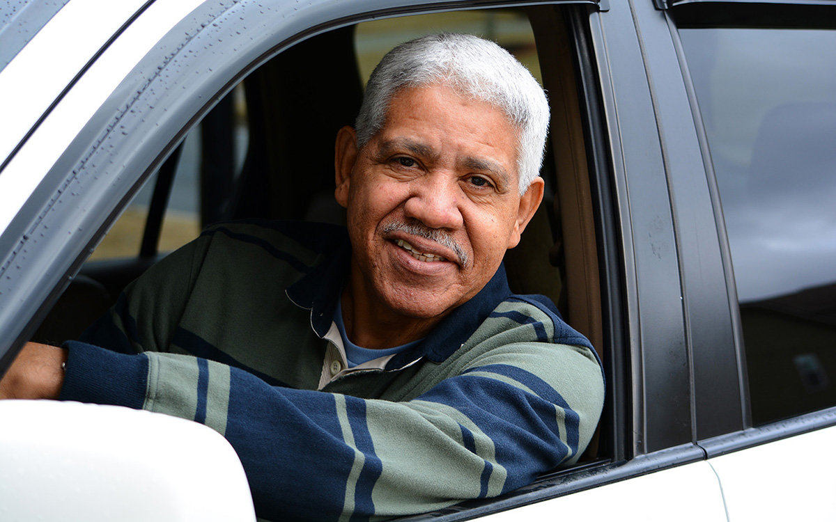 An older man sits behind the wheel of a car.