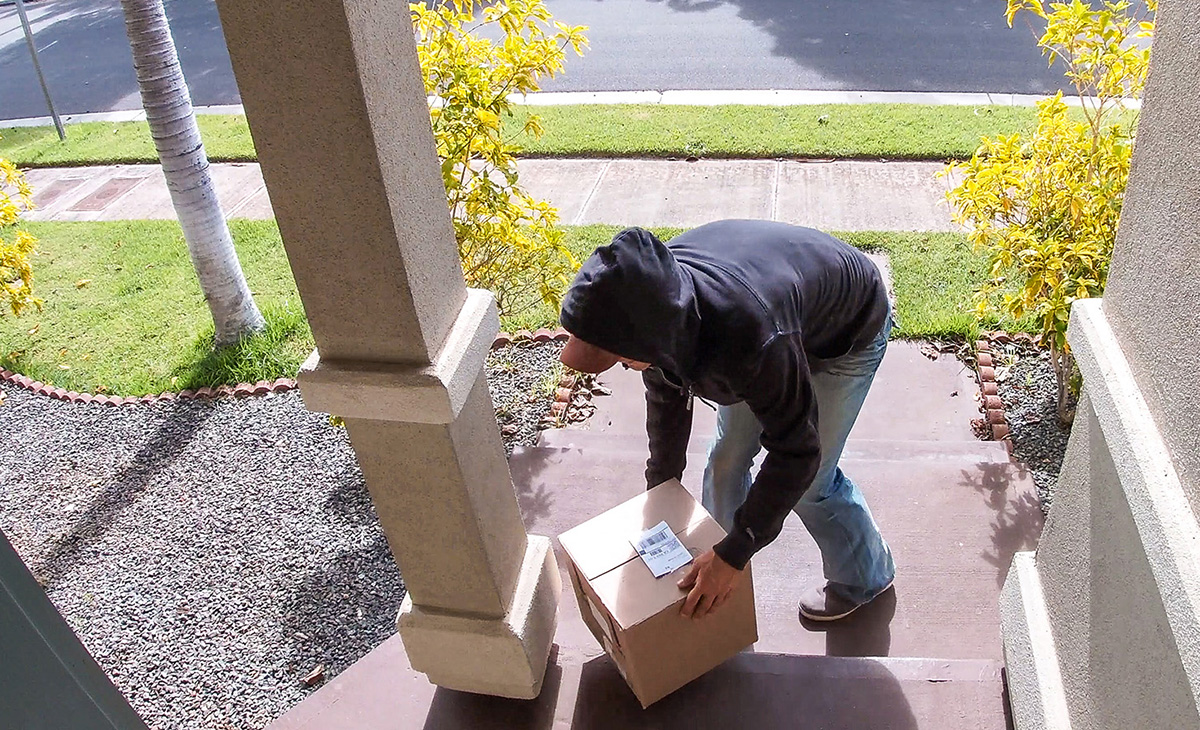 A man in a hoodie steals a package off of a front porch. 