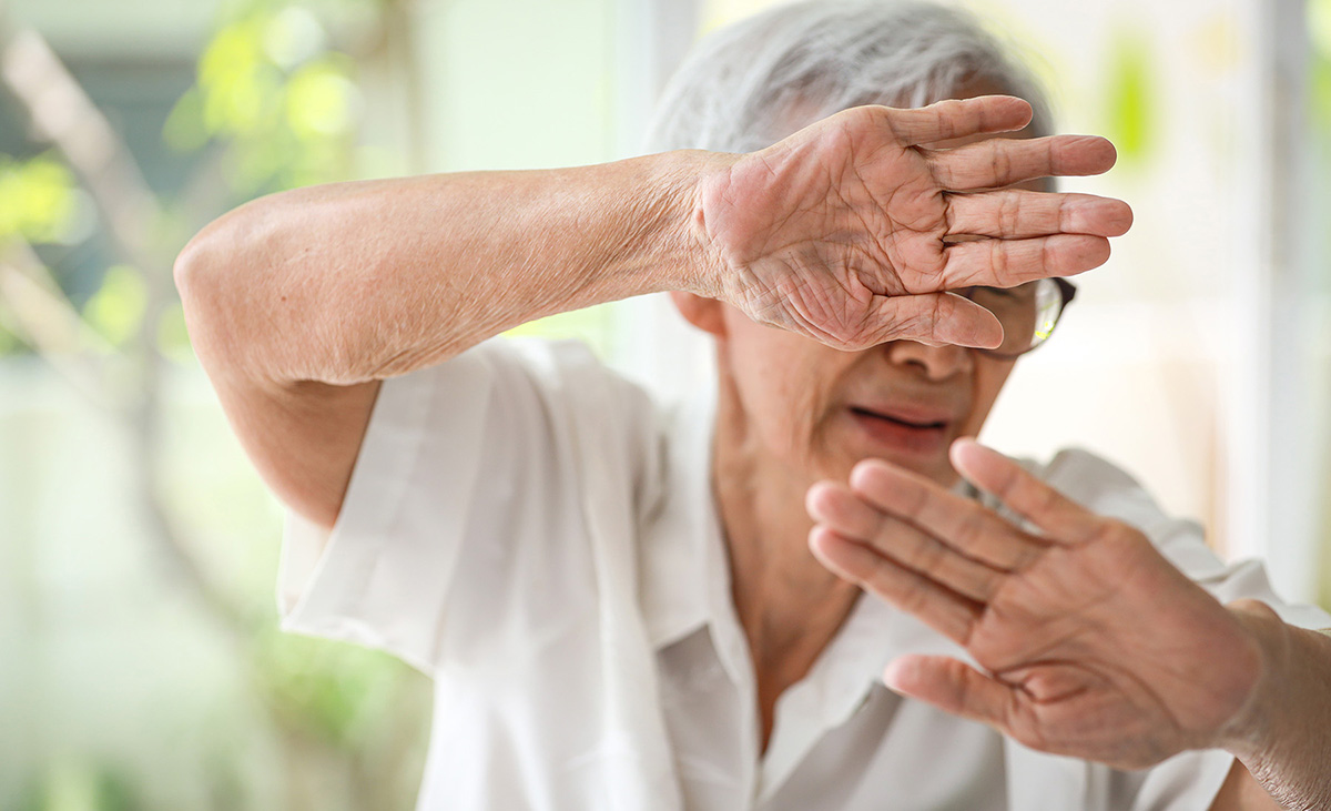 An older Asian woman shields her face with her arms in fear. 