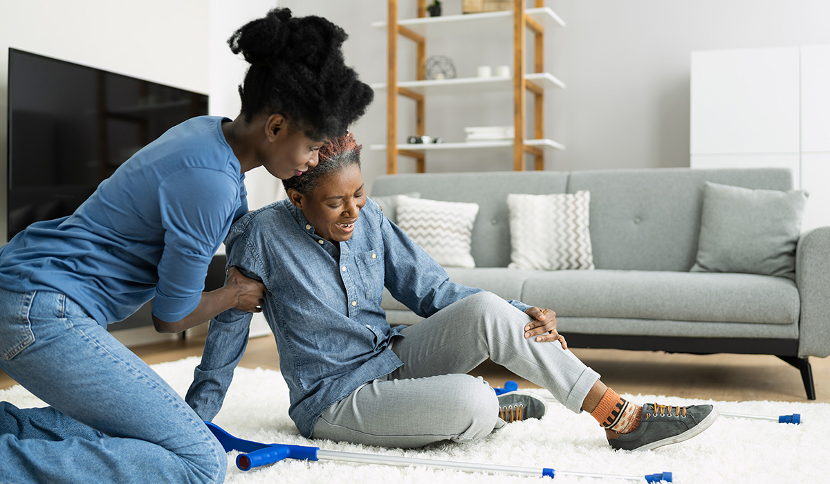 A younger woman helps an older woman seated on the floor after suffering a fall.