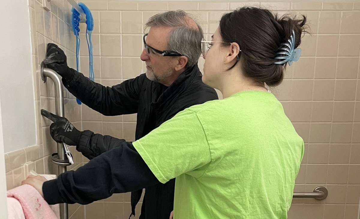 Two volunteers install a grab bar in a shower. 