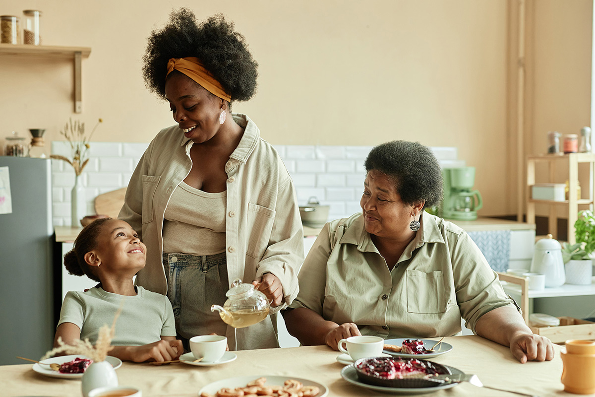 A little girl, her mom, and grandma have tea and dessert in their kitchen.