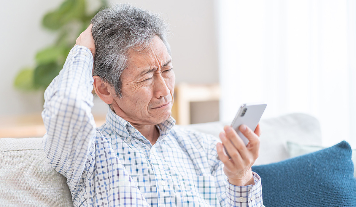 An older Asian man looks at the screen of his smartphone in confusion.