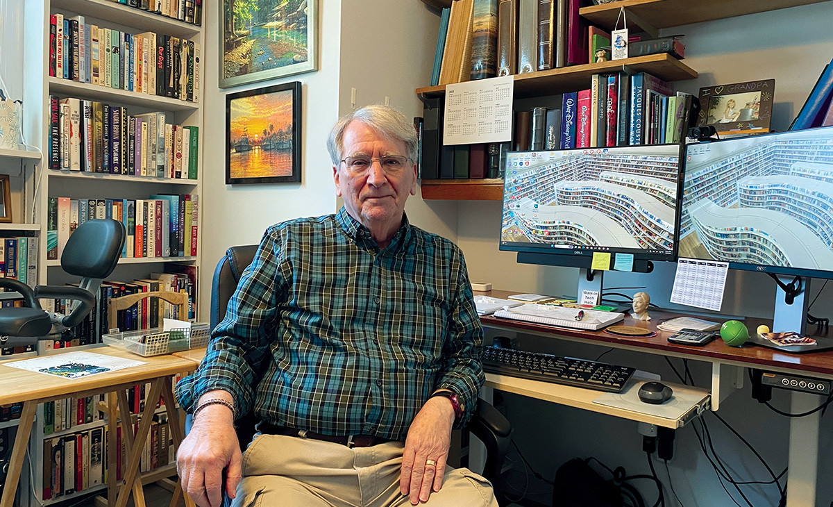 Steve Lebo seated in him home office in front of a computer with shelves of books and artwork in the background.